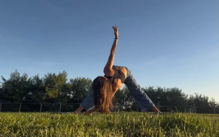 Nicole sul prato al tramonto, in una torsione con un braccio teso verso il cielo