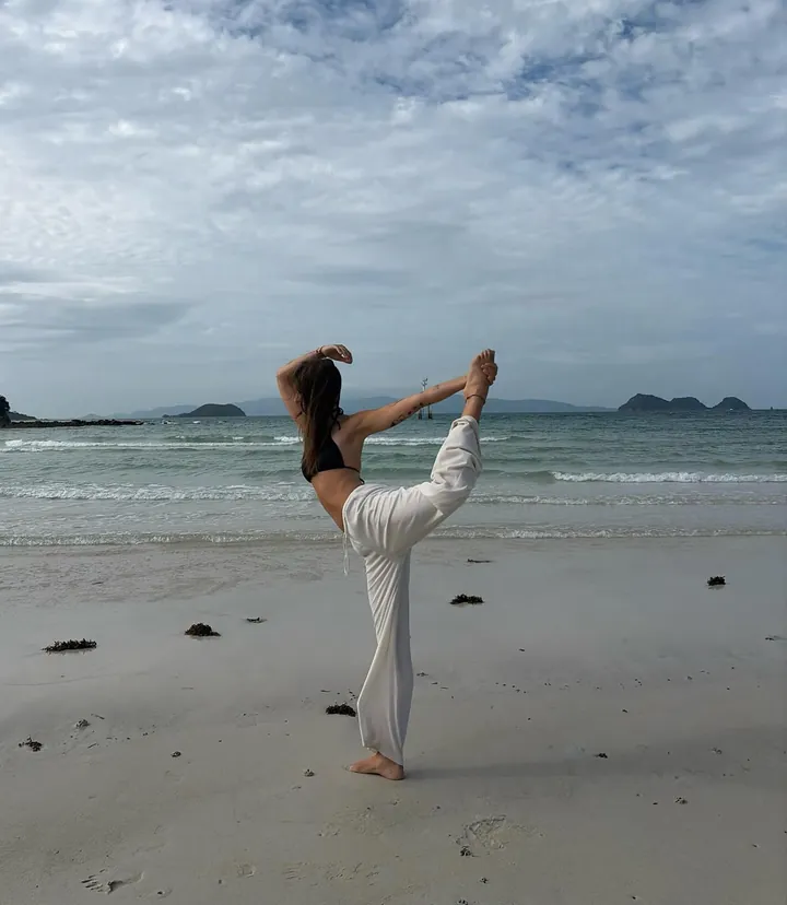 Nicole in equilibrio su una gamba sulla spiaggia, con il mare alle spalle